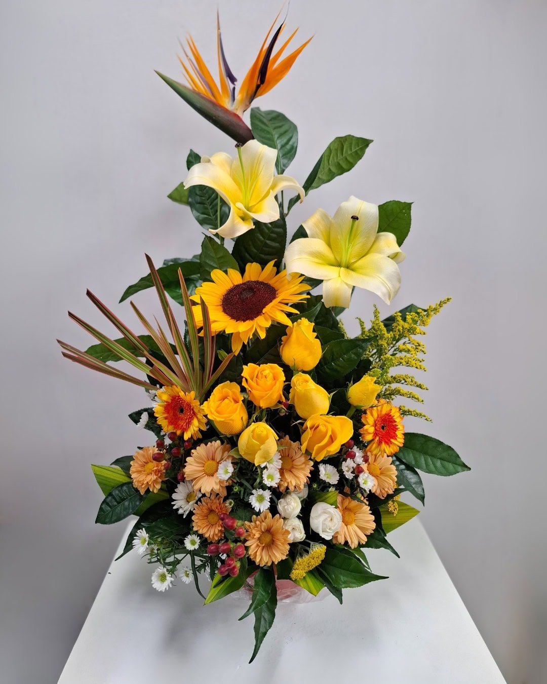 Sol Imperial – Arreglo en cerámica con lirios crema, rosas amarillas y girasol con toque tropical