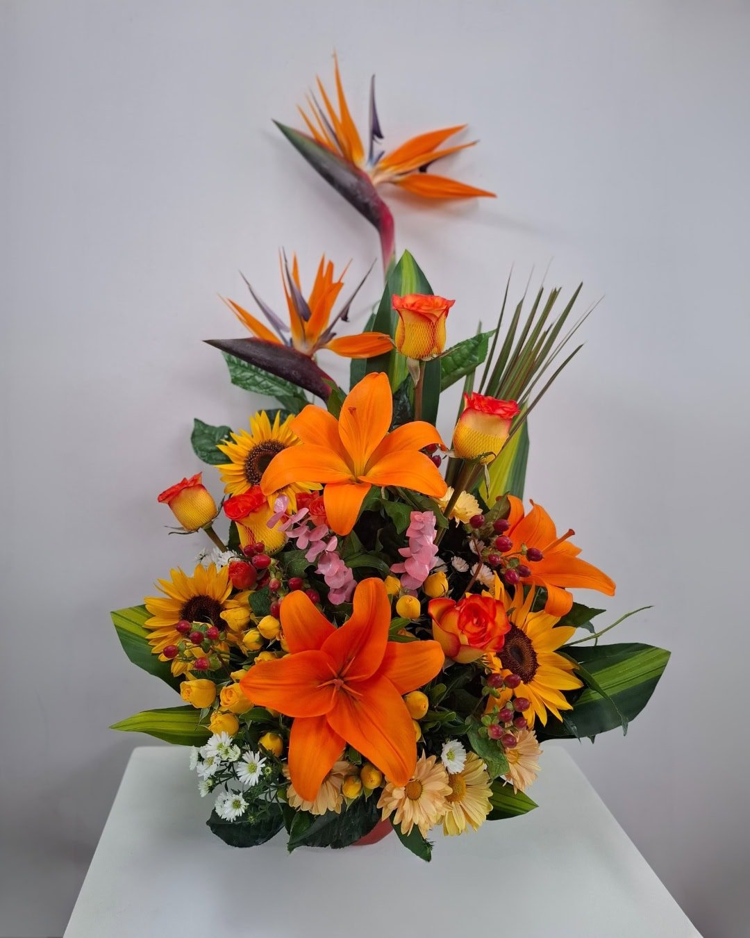 Fuego Tropical – Arreglo en cerámica con lirios naranjas, girasoles y rosas bicolor con toque exótico