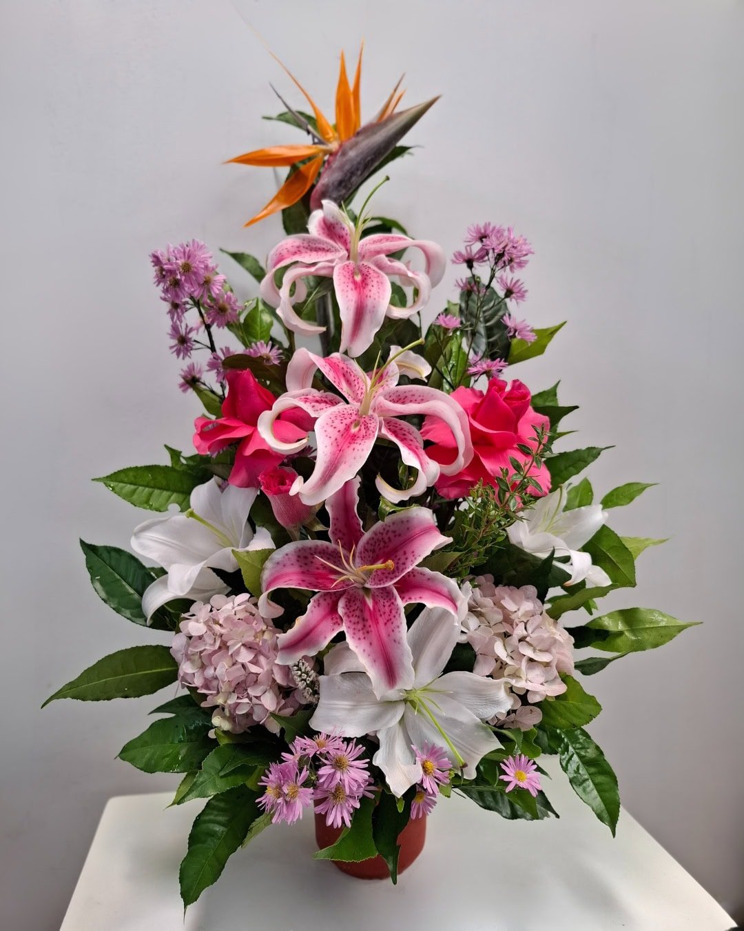 BCE-169 Orquídea del Alba – Arreglo en cerámica con lirios rosados, lirios blancos y rosas fucsia con toque exótico