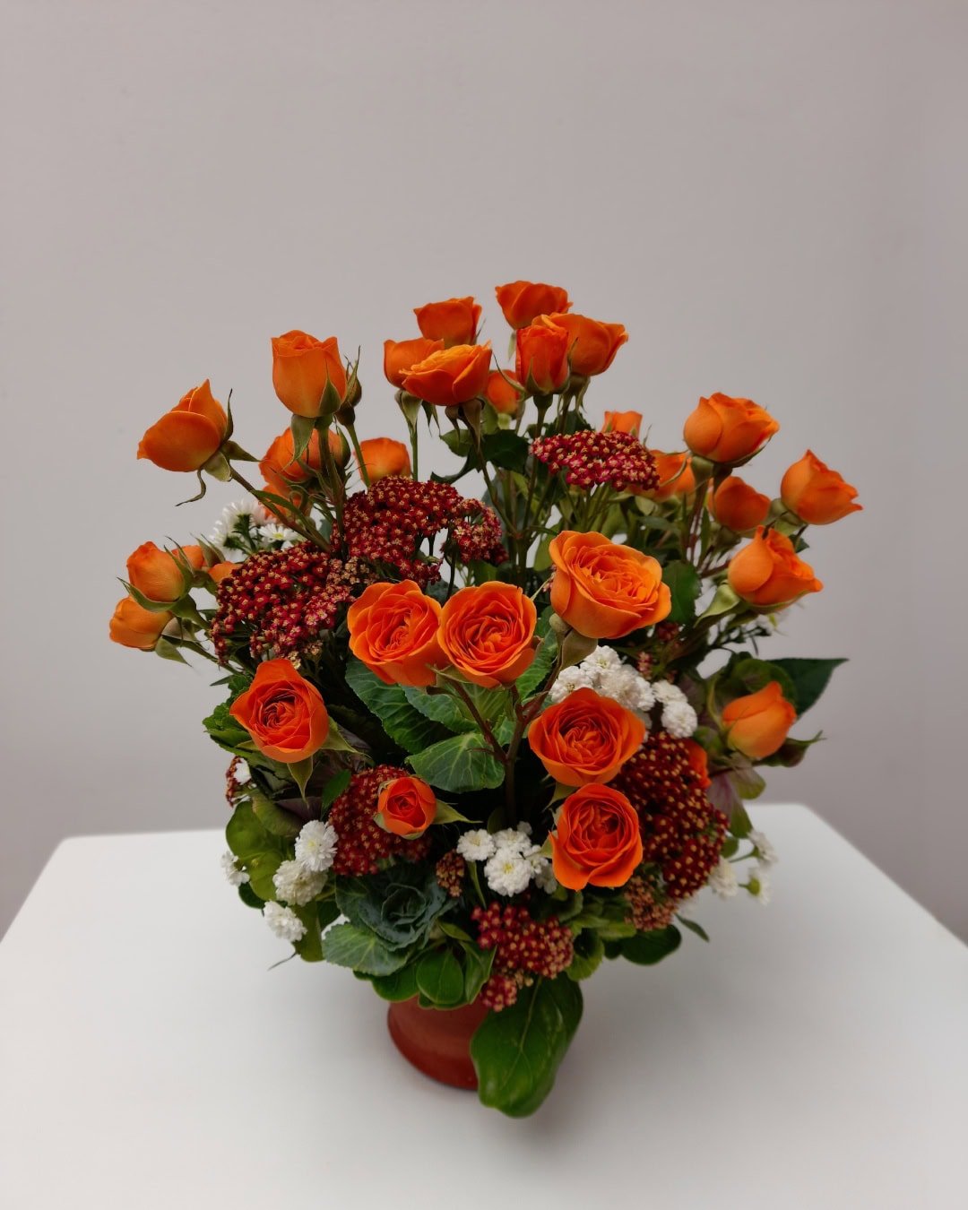 Arreglo redondo de mini rosas naranjas con acentos borgoña