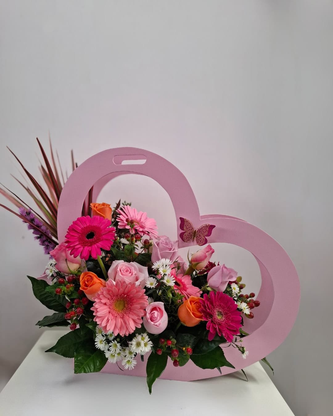 Corazón Fucsia – Arreglo en base de madera (corazón) con Gerberas rosadas y Rosas pastel, detalle vibrante