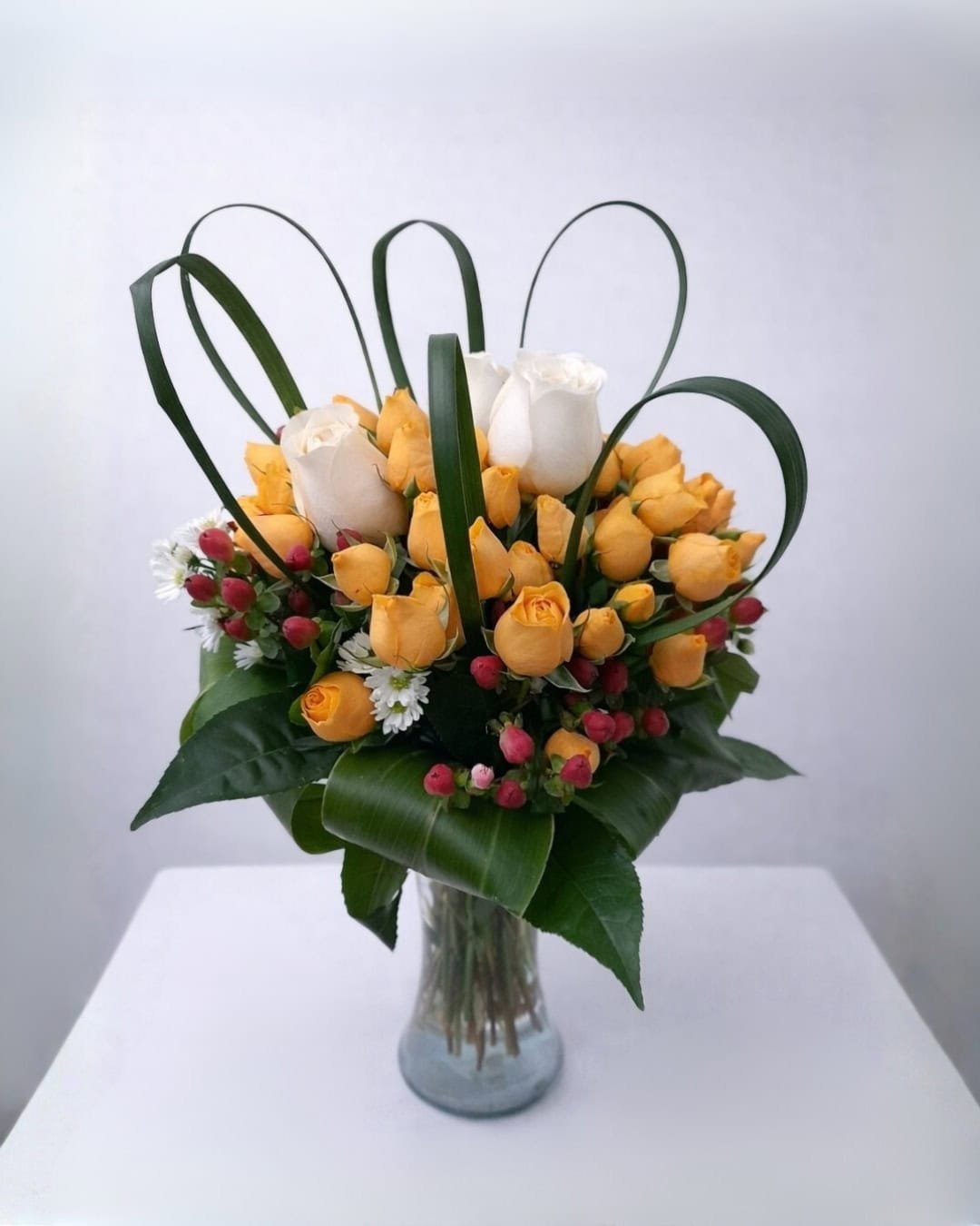 Caléndula – Florero de vidrio de mini rosas naranjas y rosas blancas con follaje arquitectónico