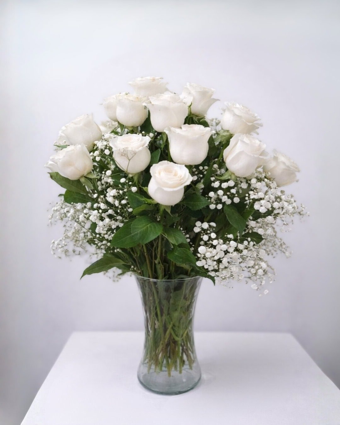 Perla – Florero de vidrio de rosas blancas con nube de gypsophila y follaje elegante