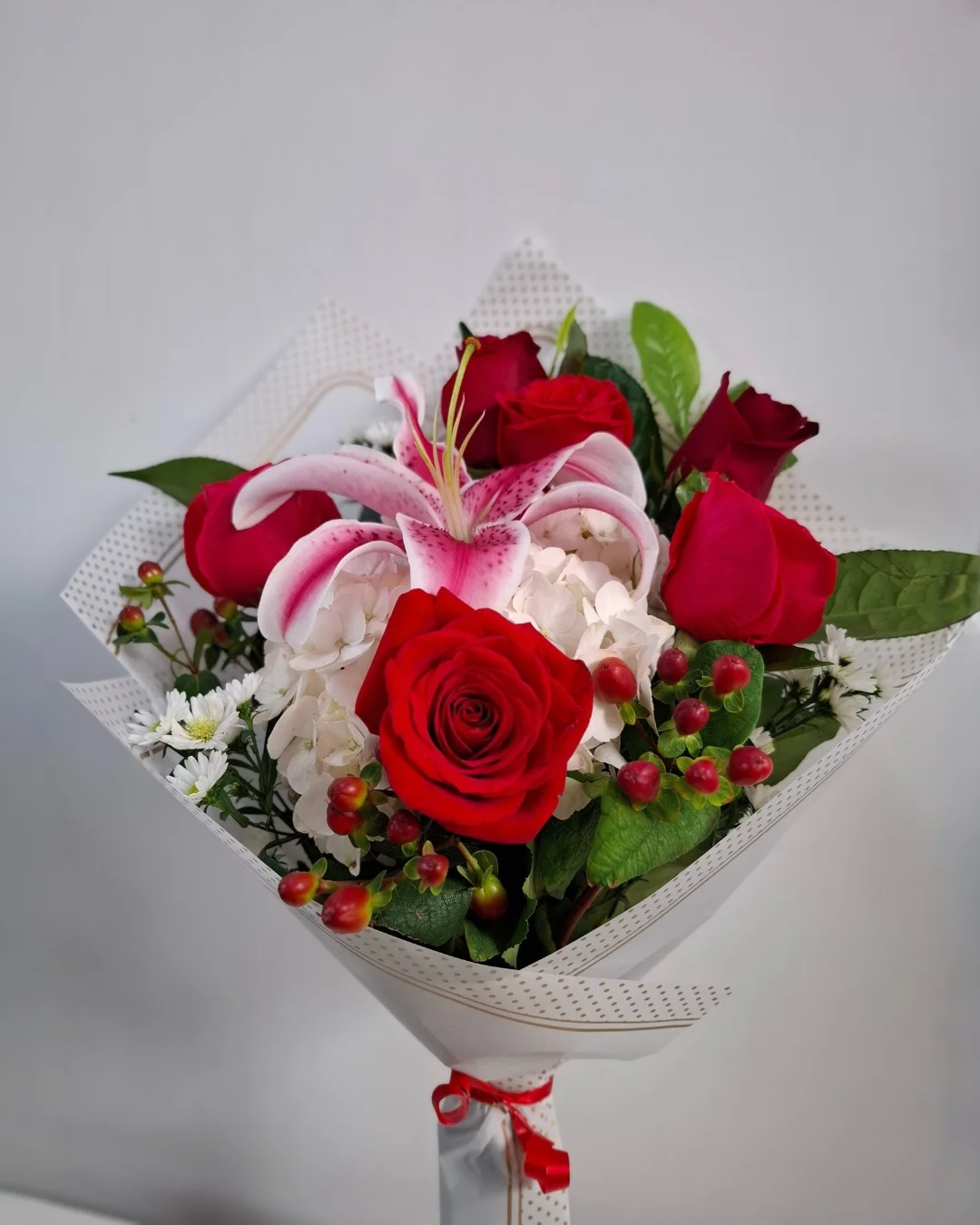 Carmesí París – Ramo floral de rosas rojas con lirio rosado, acentos blancos y follaje premium