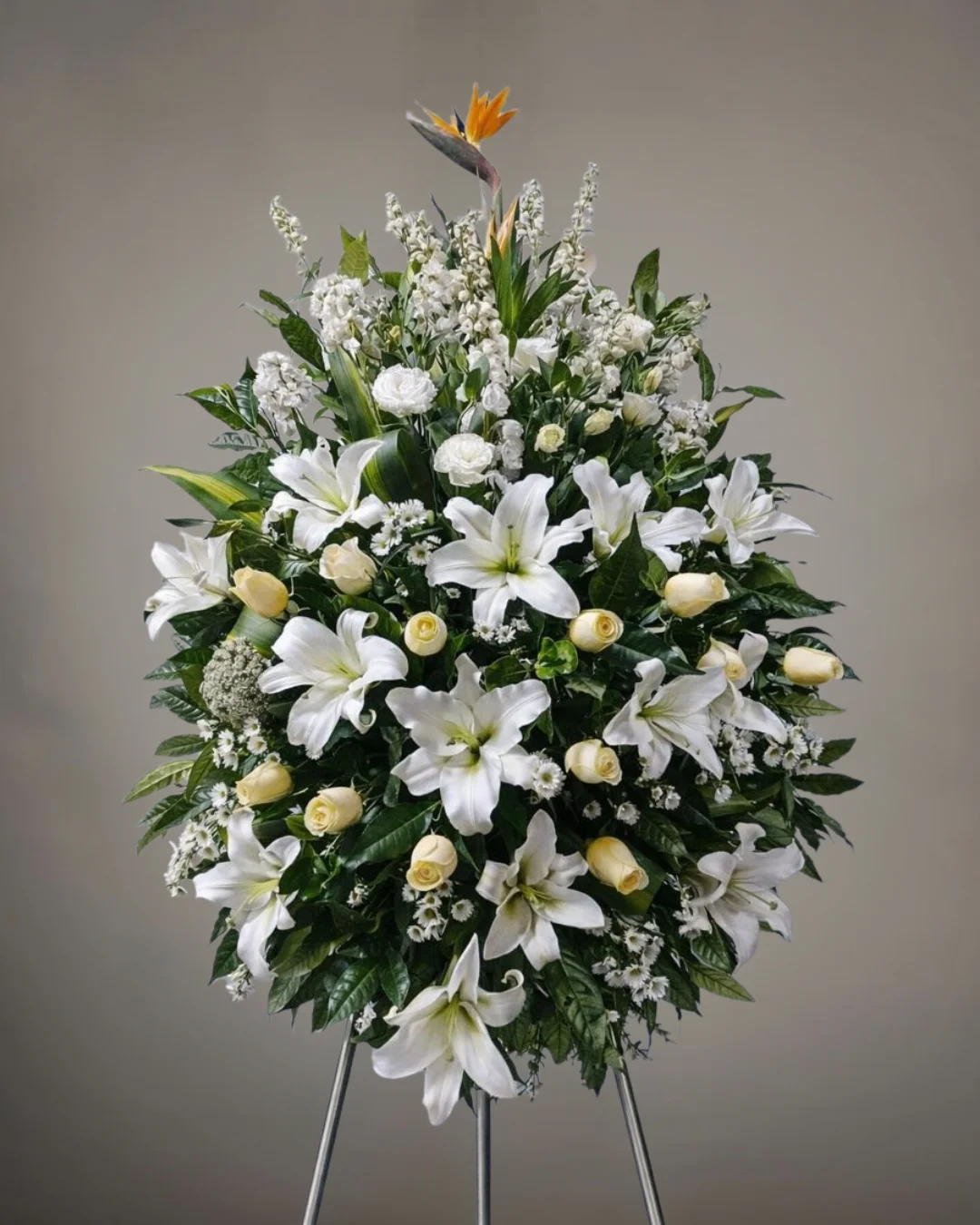 TRI-049 Cenit – Lágrima Fúnebre en Trípode de Lirios Blancos con Rosas Marfil y Ave del Paraíso Distintiva